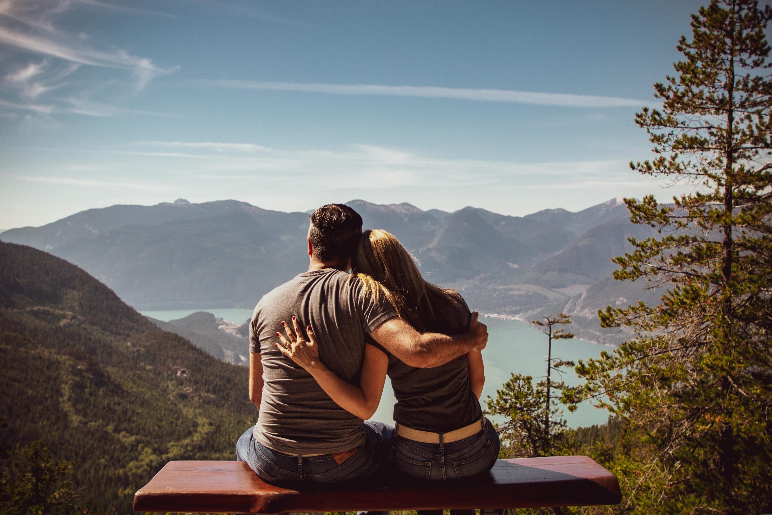 Services Couple sitting on bench embracing scenic mountain view, embodying romantic nature escape.