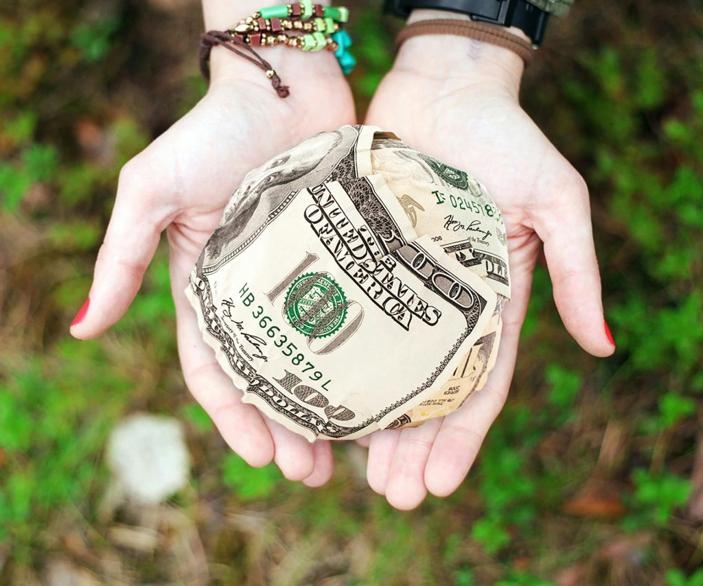 Money Spells Hands holding crumpled money outdoors, symbolizing charity and financial support.