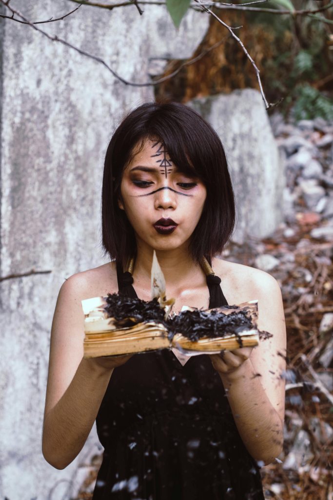Protection Spells Young woman performing witchcraft ritual with burning book outdoors.