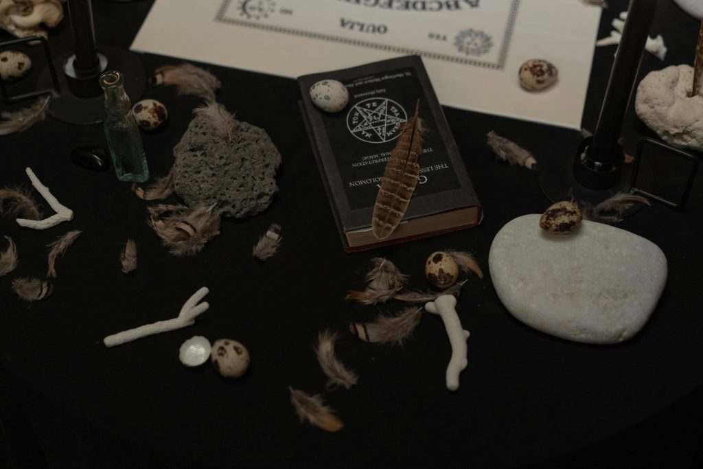Black Magic Spells A dark, mysterious scene with a book, feathers, stones, and ritualistic items.
