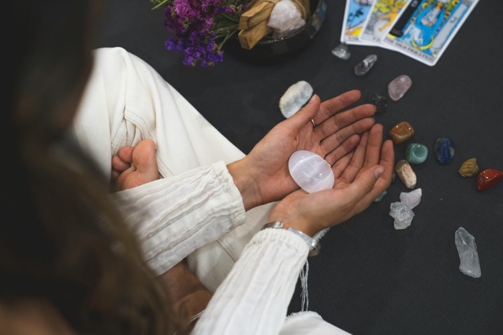 Psychic Healer A close-up top view of hands holding a crystal, surrounded by tarot cards and gemstones, symbolizing spirituality.